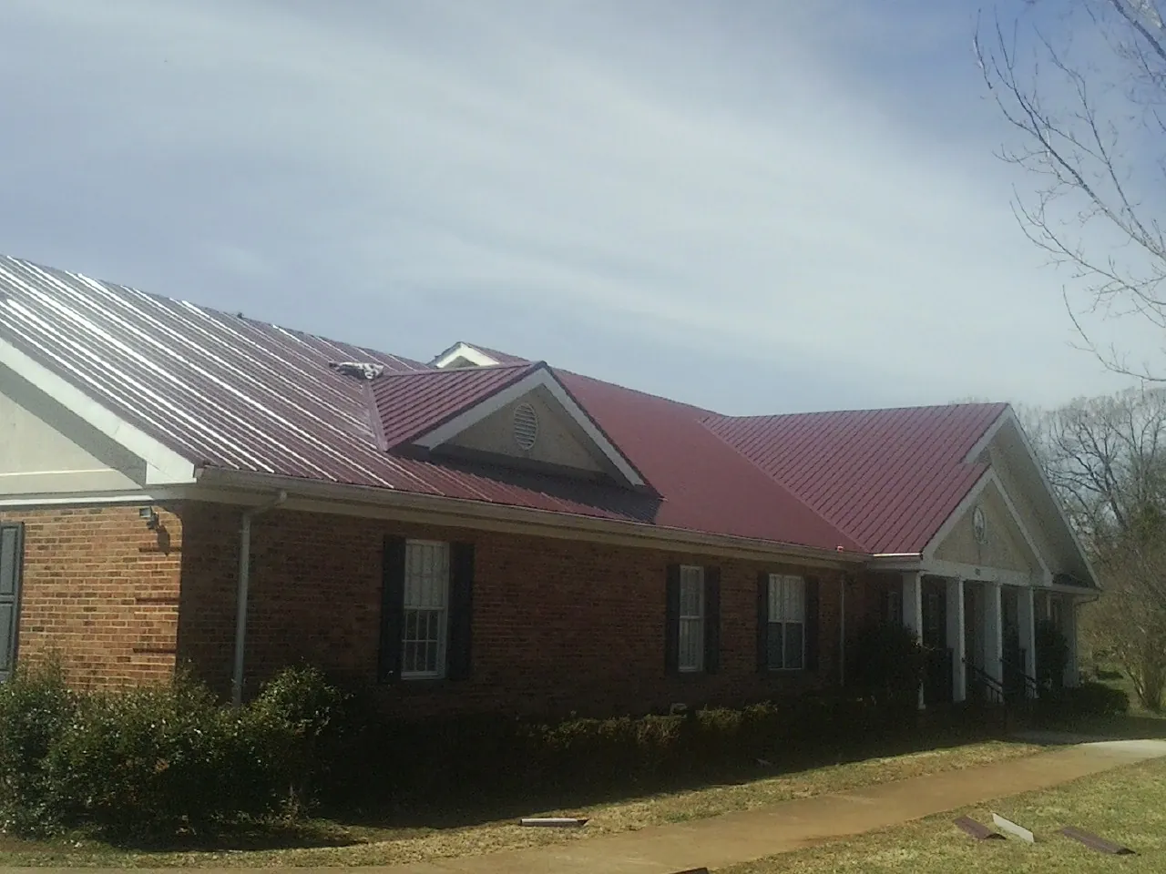 Red metal roof with gabled entries on a long brick building, from a Hail Damage Roof Repair job in Yazoo City