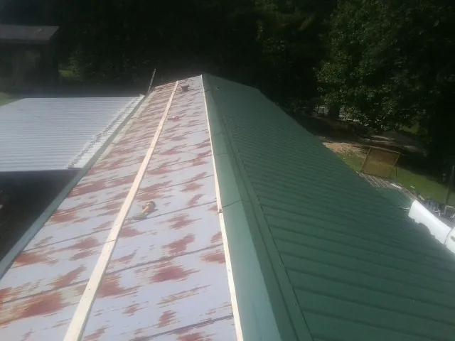 Old rusted panels beside newly installed green metal roofing — Wind Damage Roof Repair by Roofing Brothers in Yazoo City