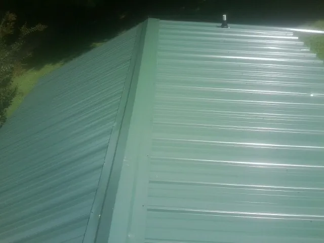 New green metal panels meeting at the ridge of a roof — Flat Roof Repair work by our crew in Yazoo City