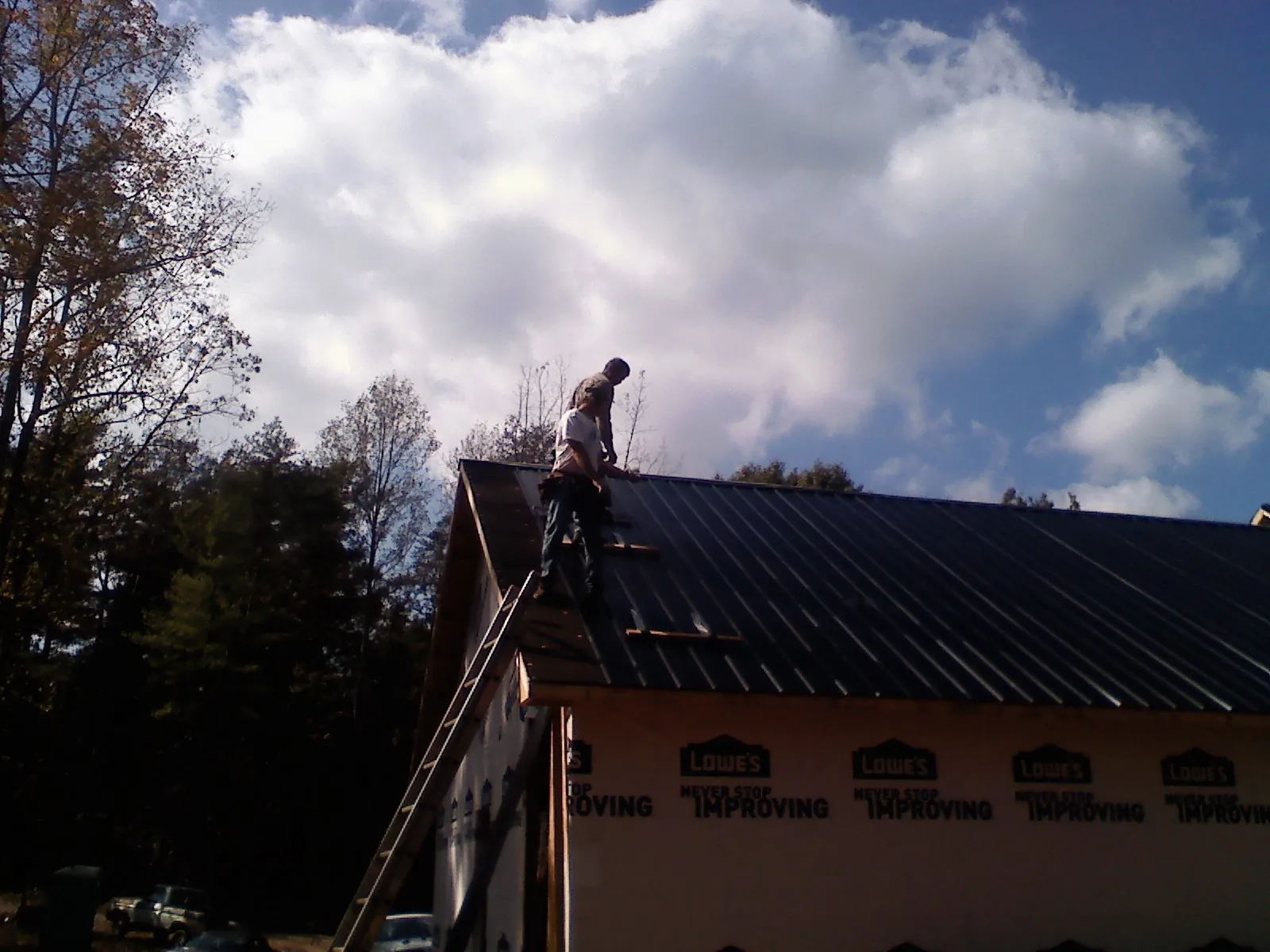 Roofer fastening dark metal panels high against a cloudy sky, from a Roof Inspection job in Yazoo City