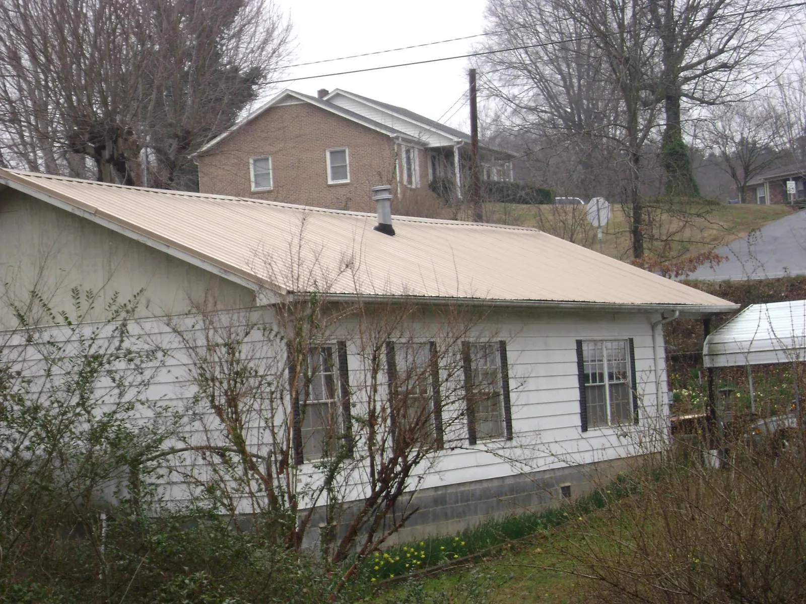Tan metal roof on a white sided house set into a hillside — Commercial Roofing by Roofing Brothers in Yazoo City
